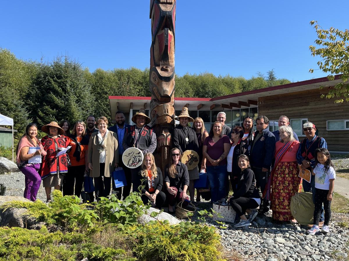Group of people standing in front of totem pole.