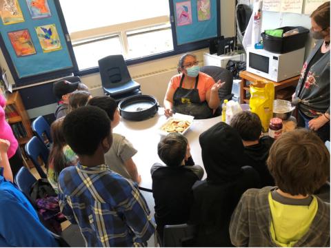 Students gather around a circular table with a teacher sitting in the center