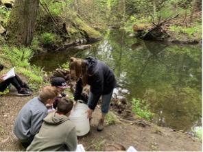 Students huddle in a group next to a pond