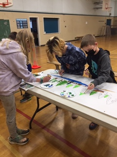 3 students work on a painting on a long table in a gym