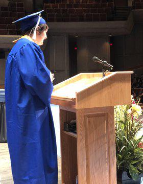 A graduate in a cap and gown give a speech at a podium
