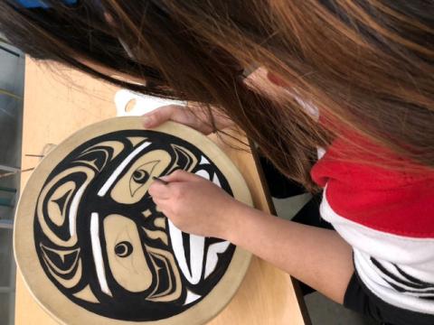 A student paints on a round piece of wood